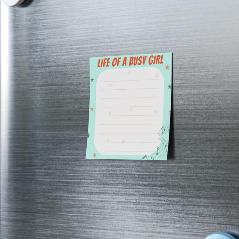 May include: A rectangular notepad with the text "LIFE OF A BUSY GIRL" in red and orange. The notepad has a light blue background with white lines for writing, star accents, and musical notes.
