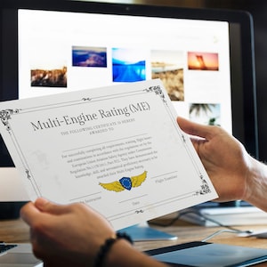 Può includere: Una persona tiene in mano un certificato di abilitazione multimotore (ME). Il certificato ha un bordo decorativo e il testo "Multi-Engine Rating (ME)". Lo sfondo include uno schermo di computer che mostra immagini.