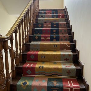 May include: A long, multi-colored stair runner rug featuring a patchwork design with various geometric patterns in shades of red, yellow, blue, green, and brown. The runner is secured to dark wooden stairs with horizontal brass stair rods.