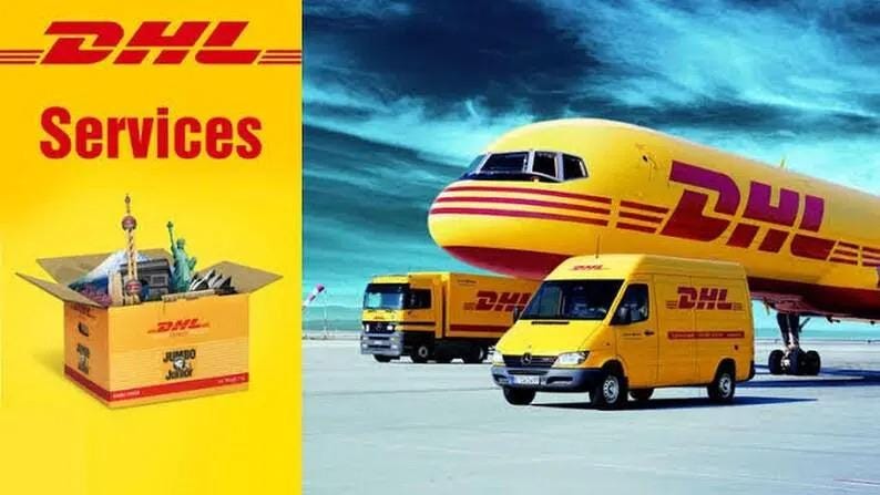 Puede incluir: Una caja de env&iacute;o amarilla de DHL llena de monumentos en miniatura se encuentra junto a un avi&oacute;n de carga amarillo de DHL y dos camiones de reparto amarillos de DHL en una pista. El texto DHL y Services est&aacute; impreso en rojo sobre fondo amarillo.