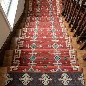 Puede incluir: Una alfombra larga y rectangular para escaleras en tono rojo intenso, con un patr&oacute;n repetitivo de formas geom&eacute;tricas de diamante en blanco y turquesa. Incluye un borde marr&oacute;n oscuro con motivos blancos y flecos en el extremo inferior.
