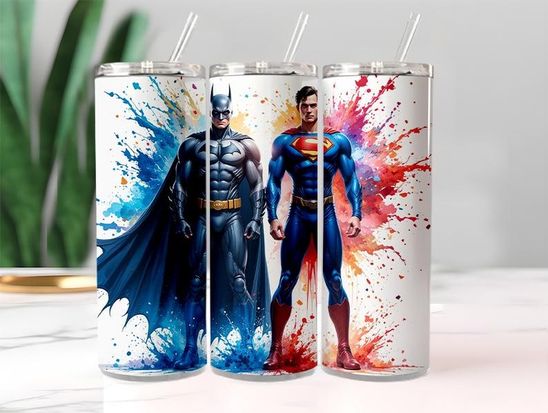 Puede incluir: Tres vasos de acero inoxidable blancos con pajitas transparentes. Cada vaso presenta un dise&ntilde;o de superh&eacute;roe: Batman con un traje y capa azul oscuro, y Superman con un traje azul con el logo "S" rojo. El fondo tiene salpicaduras de pintura coloridas.