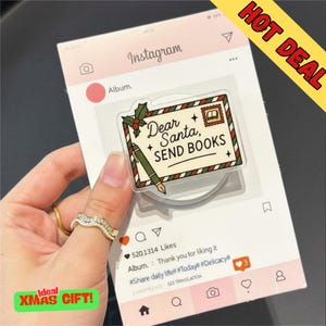 May include: A clear acrylic phone grip with a design resembling a letter to Santa, reading "Dear Santa, SEND BOOKS." The grip is set against a pink Instagram-style background with a "Hot Deal" sticker. A green "Ideal Xmas Gift!" sticker is also present.