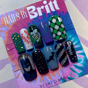 Pode incluir: Um conjunto de dez unhas postiças com vários designs, incluindo Batman, Joker e padrões abstratos. As unhas apresentam cores como verde, branco, preto e prata, algumas adornadas com strass. O texto "NAILS BY Britt" é visível.