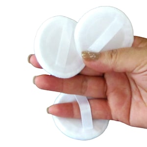 May include: Three white round powder puffs with white ribbon ties. The puffs are soft and fluffy.