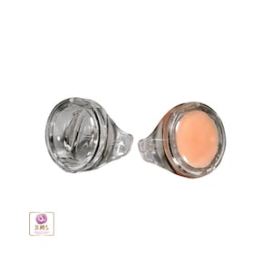 May include: Two clear plastic rings with a round, flat top. One ring has a clear top, and the other ring has a peach-colored top.