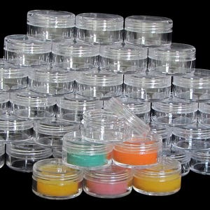 May include: A large stack of clear plastic containers with lids. The containers are arranged in a pyramid shape. There are four smaller containers in the front, filled with different colored substances.