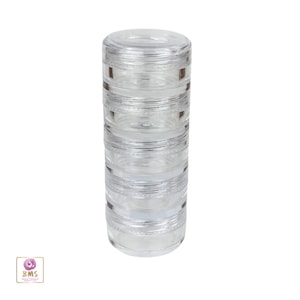 May include: A clear, stackable cosmetic container with multiple compartments. The cylindrical design features several transparent sections that screw together, creating a compact storage solution. The container is made of clear plastic.