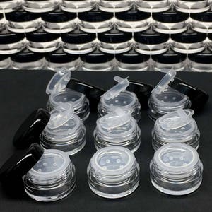 May include: Ten clear plastic jars with black lids and sifter tops. The jars are arranged in two rows of five. The jars are empty and ready to be filled with powder.