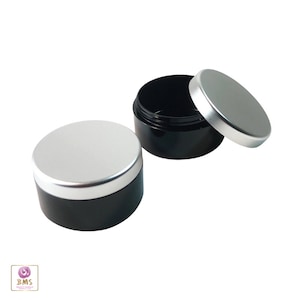 May include: Two black plastic containers with silver lids. The containers are round and have a smooth surface. The lids are also round and have a smooth surface.