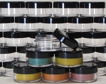 May include: A stack of clear plastic jars with black lids. The jars are filled with different colored creams or lotions. The jars are arranged in a pyramid shape.