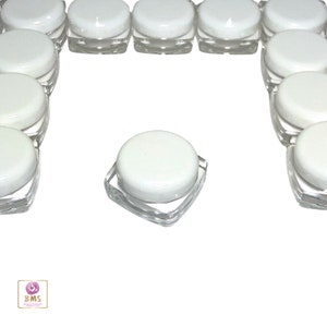 May include: A group of 15 clear plastic jars with white lids. The jars are arranged in a semi-circle shape, with one jar in the center.