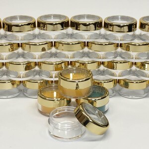 May include: A stack of clear plastic containers with gold lids. The containers are stacked in a pyramid shape. The containers are small and round.
