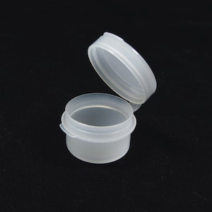 May include: A clear plastic container with a lid. The container is small and round, and the lid is slightly larger than the container. The container is open and the lid is resting on the side.