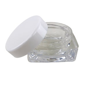 May include: A clear plastic jar with a white lid. The jar has a square shape with rounded edges. The lid is round and has a smooth surface.