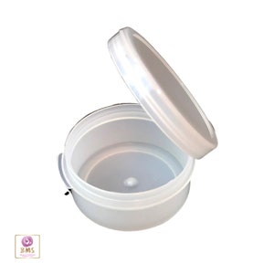 May include: A clear plastic round container with a lid. The lid is open and the container is empty.