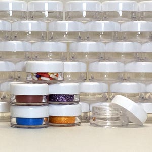 May include: A stack of clear plastic containers with white lids. The containers are filled with various colorful items, including sprinkles, glitter, and paint.