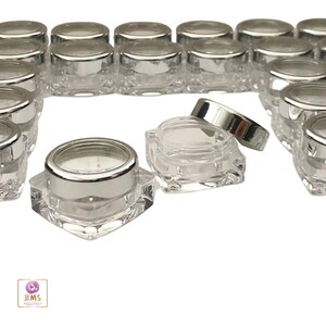 May include: A group of clear plastic square containers with silver lids. The containers are small and perfect for storing small items like lip balm, eye cream, or other cosmetics.
