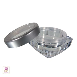 May include: A clear plastic square container with a silver lid. The lid has a clear plastic window on top. The container is empty.