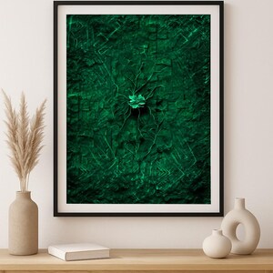 Könnte beinhalten: Gerahmter abstrakter Kunstdruck mit strukturiertem, dunkelgrünem Hintergrund und einer zentralen, stilisierten Blume. Das Kunstwerk hat eine moderne Ästhetik mit einem schwarzen Rahmen. Es wird auf einem hellen Holztisch ausgestellt.