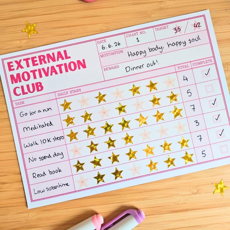 May include: A rectangular paper habit tracker titled External Motivation Club with pink borders. It features rows for tasks like Go for a run and Meditated, with gold star stickers for progress, a target of 35 out of 42, and a reward of Dinner out.