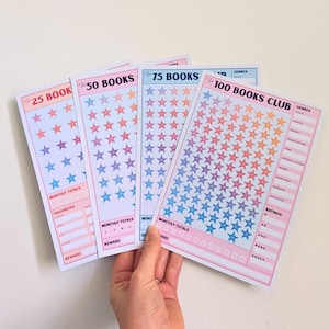 May include: Four rectangular paper reading trackers with pink borders, featuring rows of coloured stars and text labels including 25 Books, 50 Books, 75 Books, and 100 Books Club. Each sheet includes sections for monthly totals, genres, and ratings.