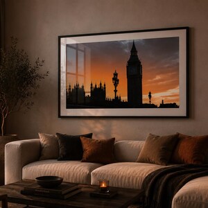 Könnte beinhalten: Ein großes, rechteckiges gerahmtes Wandbild mit der Silhouette des Big Ben Uhrturms und des Palace of Westminster vor einem orangefarbenen und dunkelblauen Sonnenuntergangshimmel, platziert über einem beigen Sofa in einem Wohnzimmer.