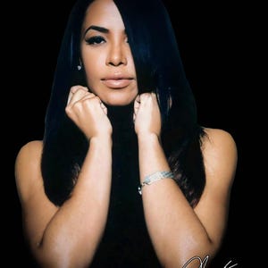 May include: A portrait of a person with long, dark hair and a black turtleneck. The person is looking directly at the camera, with their hands near their face. A silver bracelet is visible on their wrist. The background is black.