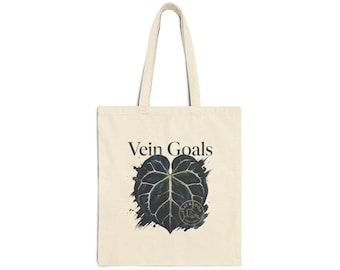 May include: A beige canvas tote bag featuring the text Vein Goals in black lettering above a dark green heart-shaped leaf illustration with prominent white veins and a small circular Leaf & Loom New York logo stamp on the lower right side.