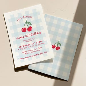 Puede incluir: Dos invitaciones plegadas con un patrón de cuadros vichy azul claro. La invitación frontal dice "It's Elsie's cherry first birthday" con detalles del evento. Una ilustración de cereza está en la parte superior. La parte posterior de la invitación tiene una ilustración de cereza.