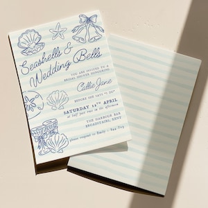 May include: A folded invitation with a light blue striped design and blue illustrations of seashells and bells. The text reads "Seashells & Wedding Bells" and invites guests to a bridal shower for Callie Jane.