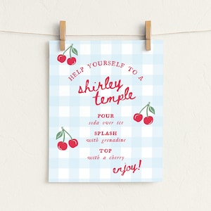 May include: A recipe card for a Shirley Temple cocktail, hanging by a wooden clip. The card has a light blue gingham pattern background. Red text reads "Help yourself to a Shirley Temple" with instructions and cherry illustrations.