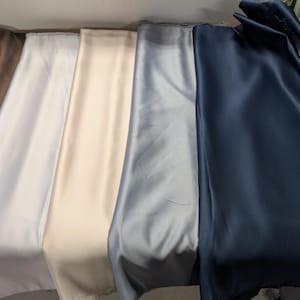 Puede incluir: Una colecci&oacute;n de telas plegadas en varios colores, incluyendo rojo, marr&oacute;n, blanco, crema, gris y azul marino. Las telas tienen una textura suave y sedosa y est&aacute;n dispuestas una al lado de la otra, mostrando sus diferentes tonos y brillo.
