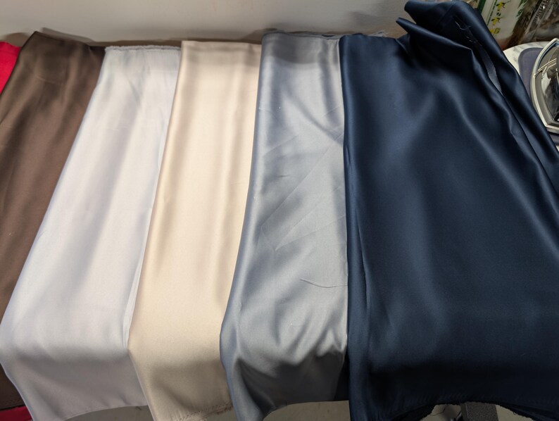 Puede incluir: Una colecci&oacute;n de telas plegadas en varios colores, incluyendo rojo, marr&oacute;n, blanco, crema, gris y azul marino. Las telas tienen una textura suave y sedosa y est&aacute;n dispuestas una al lado de la otra, mostrando sus diferentes tonos y brillo.