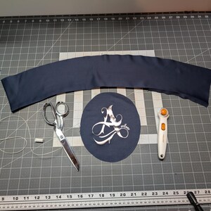 Puede incluir: Un trozo de tela azul marino, tijeras, un cortador rotatorio, un trozo de tela redondo con un dise&ntilde;o plateado, hilo y una barra de tiza blanca est&aacute;n dispuestos sobre una esterilla de corte gris. Los art&iacute;culos sugieren un proyecto de costura o manualidades.