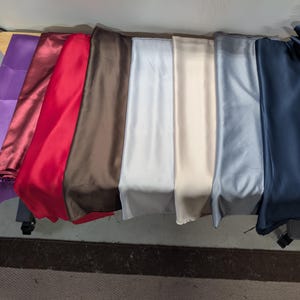 Puede incluir: Una colecci&oacute;n de telas plegadas en varios colores, incluyendo morado, burdeos, rojo, marr&oacute;n, blanco, beige, gris y azul marino. Las telas parecen ser de sat&eacute;n o un material liso similar, dispuestas sobre una mesa.