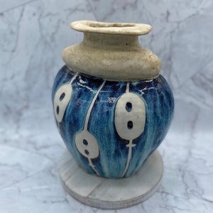 May include: A blue and white ceramic vase with a unique design. The vase has a rounded body with a white rim and a white design of stylized flowers.