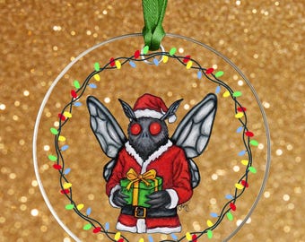 Puede incluir: Adorno navideño redondo y transparente con un personaje de tipo polilla de dibujos animados vestido con un traje y gorro de Papá Noel, sosteniendo una caja de regalo verde. El adorno está rodeado por una guirnalda de luces navideñas multicolores y tiene una cinta verde para colgar.