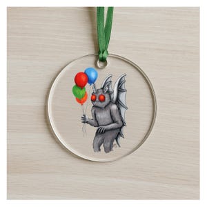 Puede incluir: Adorno navideño redondo y transparente con una cinta verde. Representa un hombre polilla de dibujos animados con ojos rojos y alas, sosteniendo globos. Los globos son rojos, azules, verdes y naranjas. Ideal para colgar y decorar.