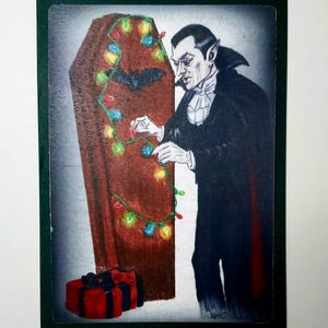 Könnte beinhalten: Illustration von Dracula, der einen Sarg mit Weihnachtsbeleuchtung schmückt. Dracula trägt einen schwarzen Umhang und Smoking. Eine rote Geschenkbox mit schwarzer Schleife befindet sich im Vordergrund. Das Bild hat einen grünen Rand.