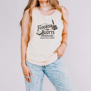 May include: A cream-colored tank top with the text "Flourish and Blotts - Booksellers - Diagon Alley, London" in black. The graphic includes a quill, books, and a scroll. The person is wearing light blue jeans.