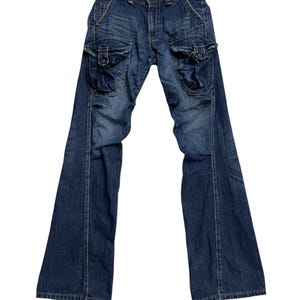 Puede incluir: Pantalones cargo de mezclilla azul con múltiples bolsillos y diseño de pernera acampanada. Los pantalones tienen un estilo clásico de cinco bolsillos con bolsillos cargo adicionales en los muslos. La mezclilla tiene un lavado descolorido.