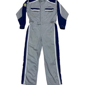May include: A gray jumpsuit with navy blue accents on the shoulders and sleeves. The jumpsuit features white stripes down the sides of the legs and a small patch on the left sleeve. It has two chest pockets and a belt at the waist.