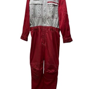 Puede incluir: Mono de carreras rojo y plateado con el logo de Nissan y un parche. El mono tiene cuello alzado, dos bolsillos en el pecho y cierre de cremallera. Las mangas y perneras son largas, y el mono parece estar hecho de un material duradero.