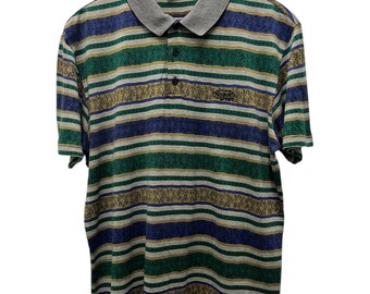 Puede incluir: Un polo vintage con rayas horizontales azules, verdes y doradas. La camisa tiene un cuello gris y el texto "MISSONI SPORT" es visible en el cuello y el pecho. La camisa está colgada en una percha de madera.