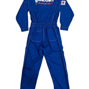 Op de afbeelding: Blauw Suzuki Technical Staff overall met witte stiksels. De overall heeft lange mouwen, een ritssluiting en het Suzuki-logo op de rug. De tekst "Technical Staff" is rood.