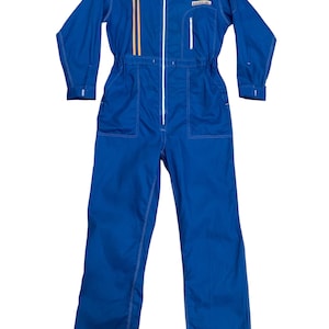 May include: A blue jumpsuit with a full-length zipper, two front pockets, and white stitching. The jumpsuit has two vertical gold stripes on the chest and a small patch on the right chest. The sleeves are long, and the waist is cinched.