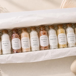 May include: A white gift box containing ten small glass bottles with cork stoppers, each filled with different bath salts. The labels read Detox, Dead Sea Salts, Rose, Energise, Relax, Himalayan Salts, Magnesium, Glow 'n' Go, Moisturising, and Revive.