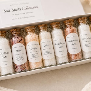 May include: A white rectangular box labelled Salt Shots Collection containing ten glass bottles filled with various bath salts. Each bottle has a cork stopper and a white label detailing the specific salt type, such as Detox, Rose, and Magnesium.