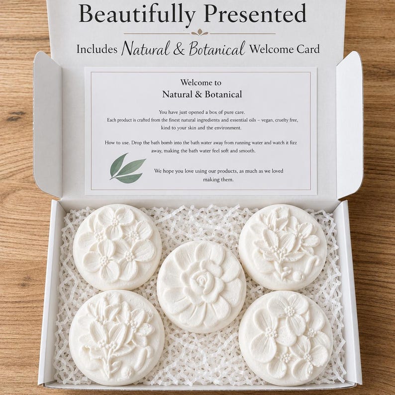 May include: An open box with six white, floral-shaped bath bombs. The box includes a welcome card with text that reads "Natural & Botanical". The bath bombs are arranged on a bed of white paper. The box is labeled "Beautifully Presented".